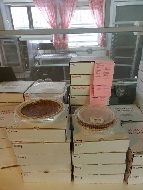 A display of various pies in clear containers on top of stacked boxes, with a menu visible in the background.