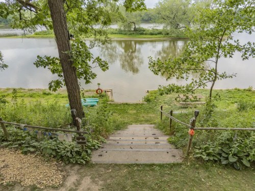 A serene riverbank scene with steps leading down to the water, surrounded by lush greenery and trees.
