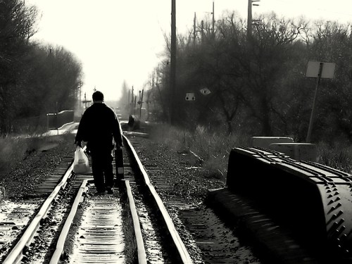 A person walks along a railway track, carrying a bag, with a foggy landscape in the background.