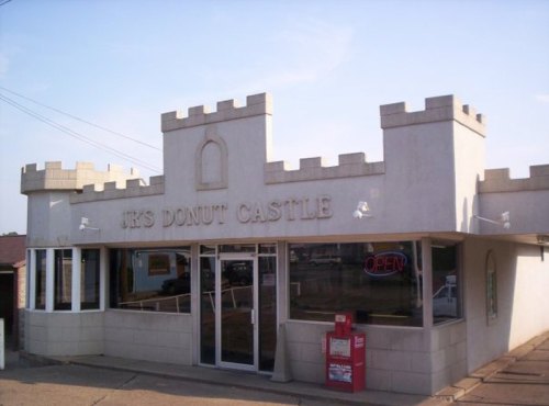 A whimsical donut shop designed like a castle, featuring a sign that reads "JR's Donut Castle" and large windows.