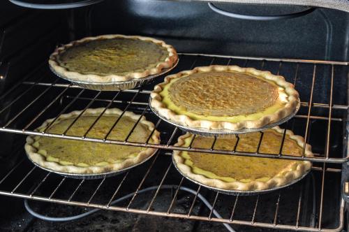 Four unbaked pies in metal crusts are placed on oven racks, ready to be baked.