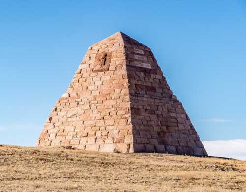 A large stone pyramid structure on a grassy landscape under a clear blue sky.