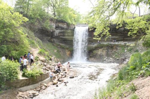 A scenic waterfall surrounded by lush greenery, with people enjoying the area near the water's edge.