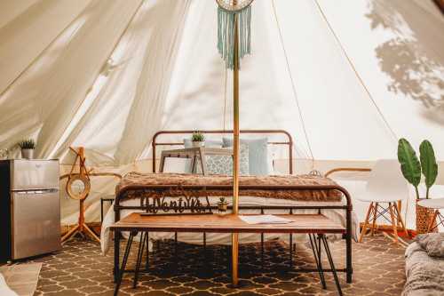 Cozy glamping tent interior featuring a bed, seating, fridge, and decorative plants. Warm, inviting atmosphere.