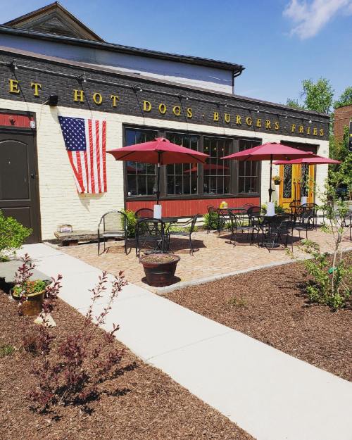 Outdoor seating area of a restaurant with red umbrellas, an American flag, and a brick pathway.