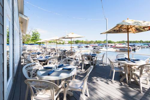 Outdoor dining area with white tables and umbrellas, overlooking a marina filled with boats under a clear blue sky.
