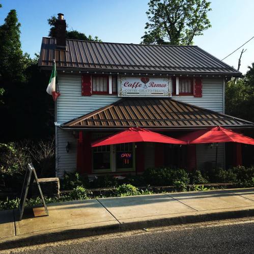 A charming café with a red and white exterior, featuring outdoor seating and an "OPEN" sign. Italian flag displayed.