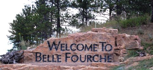 A large stone sign reading "Welcome to Belle Fourche" surrounded by trees and natural scenery.