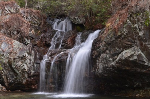 A serene waterfall cascading over rocky terrain, surrounded by lush greenery and autumn leaves.