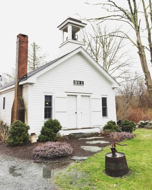 A small white building with a bell tower, labeled "No. 1," surrounded by greenery and a gravel path.