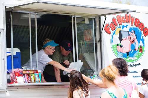 A food truck with a sign featuring a pig logo, serving customers with a woman and man at the window.