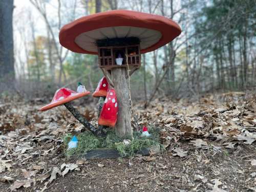 A whimsical mushroom house with red caps, surrounded by small gnomes and greenery in a forest setting.