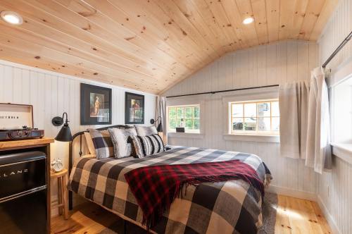 Cozy bedroom with a wooden ceiling, plaid bedding, framed art, and large windows letting in natural light.