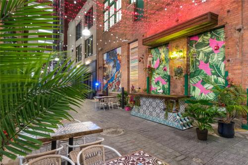 Colorful outdoor space with vibrant murals, string lights, and tropical plants, featuring tables and a bar area.