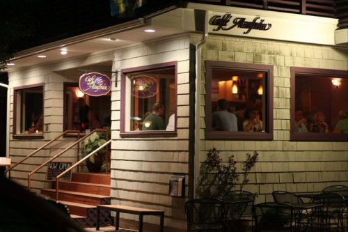 A cozy restaurant exterior at night, featuring warm lights and people dining inside.