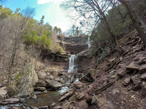 A scenic view of a waterfall cascading down rocky cliffs, surrounded by trees and a riverbed.