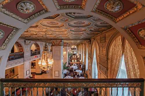 Elegant restaurant interior with ornate ceilings, chandeliers, and large windows, viewed from a balcony.