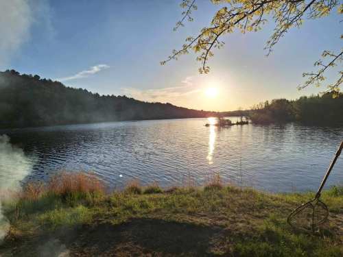 A serene lake at sunset, with trees lining the shore and gentle ripples on the water's surface.