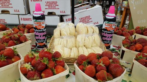 Baskets of fresh strawberries with bottles of chocolate syrup and whipped cream in a market setting.