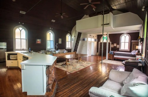 A spacious, modern interior of a converted church with wooden floors, large windows, and a cozy living area.