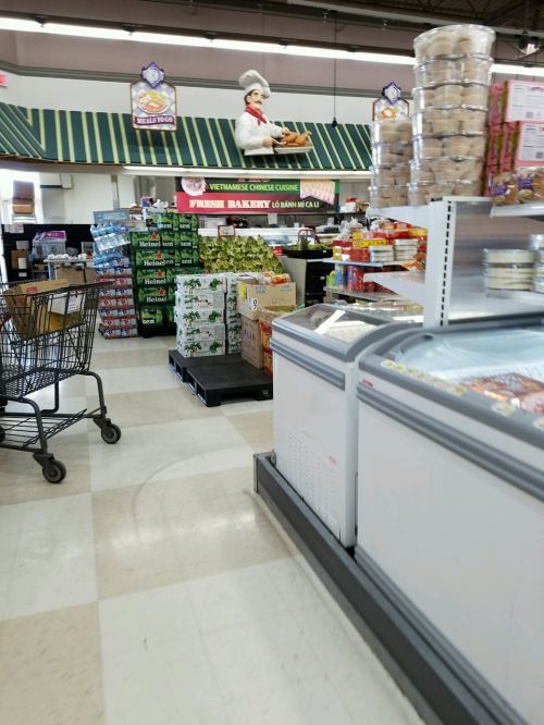 A grocery store aisle with shelves of products, a shopping cart, and a large chef figure above the display.