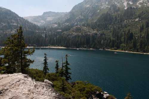 A serene lake surrounded by mountains and dense forests, with boats gently gliding on the water under a clear sky.