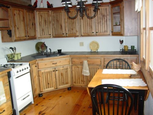 Cozy kitchen with wooden cabinets, a dining table, and a gas stove, featuring rustic decor and natural light.