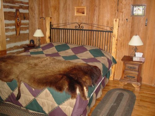 Cozy rustic bedroom with a wooden bed, quilted blanket, and a fur throw, featuring wooden walls and bedside lamps.