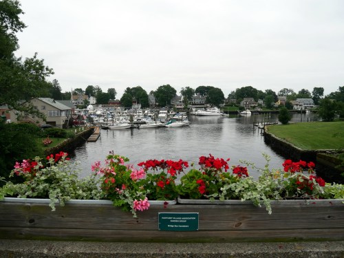 A scenic view of a marina with boats, surrounded by greenery and colorful flowers in the foreground.