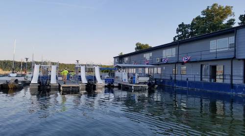 A waterfront building with two boat ramps and festive decorations, surrounded by calm water and trees in the background.