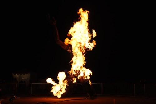 A large figure made of flames stands against a dark background, resembling a fiery sculpture or performance.