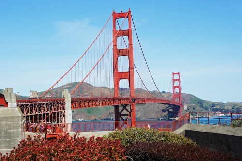 Golden Gate Bridge spans a bay, framed by greenery and hills under a clear blue sky.