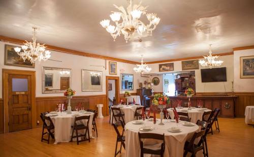 Elegant dining room with round tables, white tablecloths, and chandeliers, featuring floral centerpieces and wooden accents.