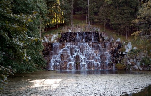A serene waterfall cascading over rocks into a calm pond, surrounded by lush greenery and trees.