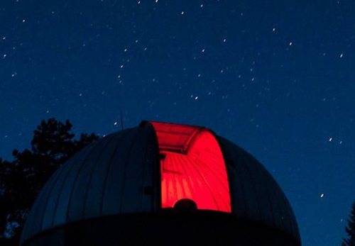 A dome-shaped observatory illuminated in red against a starry night sky.