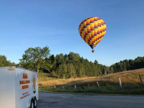 A colorful hot air balloon floats above a grassy field near a trailer for A&A Balloon Rides.