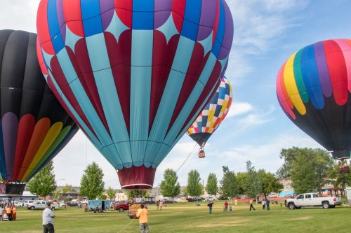 Colorful hot air balloons are inflated and ready for flight in a grassy field, with people and vehicles nearby.