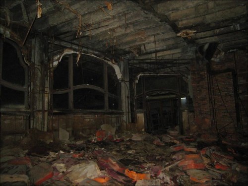 Abandoned interior of a building with crumbling walls, debris on the floor, and broken windows.