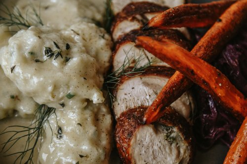 A plate featuring sliced roasted chicken, creamy mashed potatoes, roasted carrots, and purple cabbage.