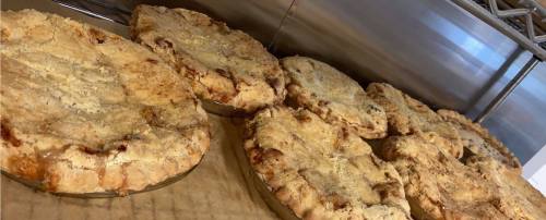 A row of freshly baked pies with golden crusts, sitting on a metal shelf.