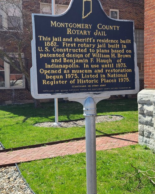Sign for Montgomery County Jail, detailing its history and significance, with a brick building and green lawn in the background.
