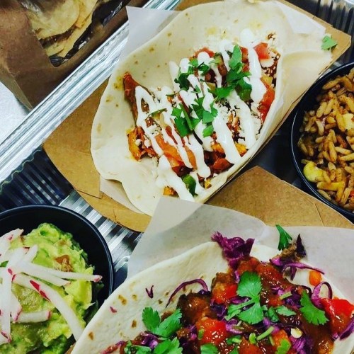 A close-up of two tacos topped with sauce and cilantro, alongside guacamole and a side of rice.