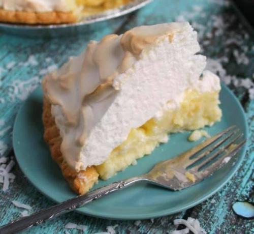 A slice of coconut cream pie on a teal plate, topped with whipped cream and a golden meringue, with a fork beside it.