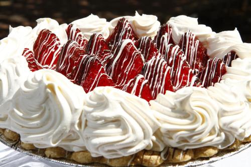 A delicious cake topped with whipped cream and a layer of glossy red strawberries, drizzled with white chocolate.
