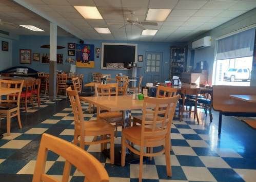 A spacious, empty dining area with wooden tables and chairs, featuring a checkered floor and blue walls.