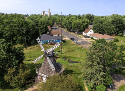 Aerial view of a windmill surrounded by greenery and houses along a quiet street.