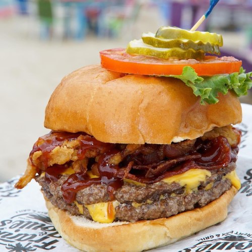 A delicious burger with a beef patty, cheese, crispy onions, bacon, lettuce, tomato, pickles, and barbecue sauce on a bun.