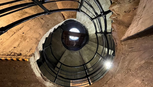 View looking up a spiral staircase with a metal railing, revealing a circular opening at the top.