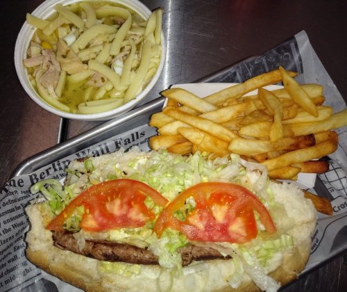 A sandwich with lettuce, tomato, and meat, served with fries and a side of pasta salad in a bowl.