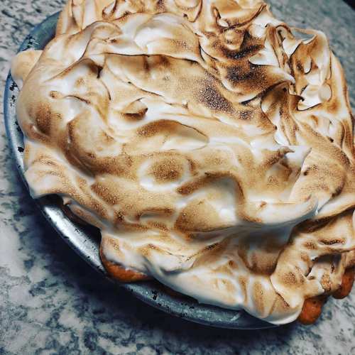 A freshly baked pie topped with golden-brown meringue, resting in a metal pie dish on a marble surface.